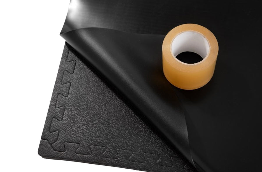 Corner of a black marley mat folded back beside a roll of floor tape